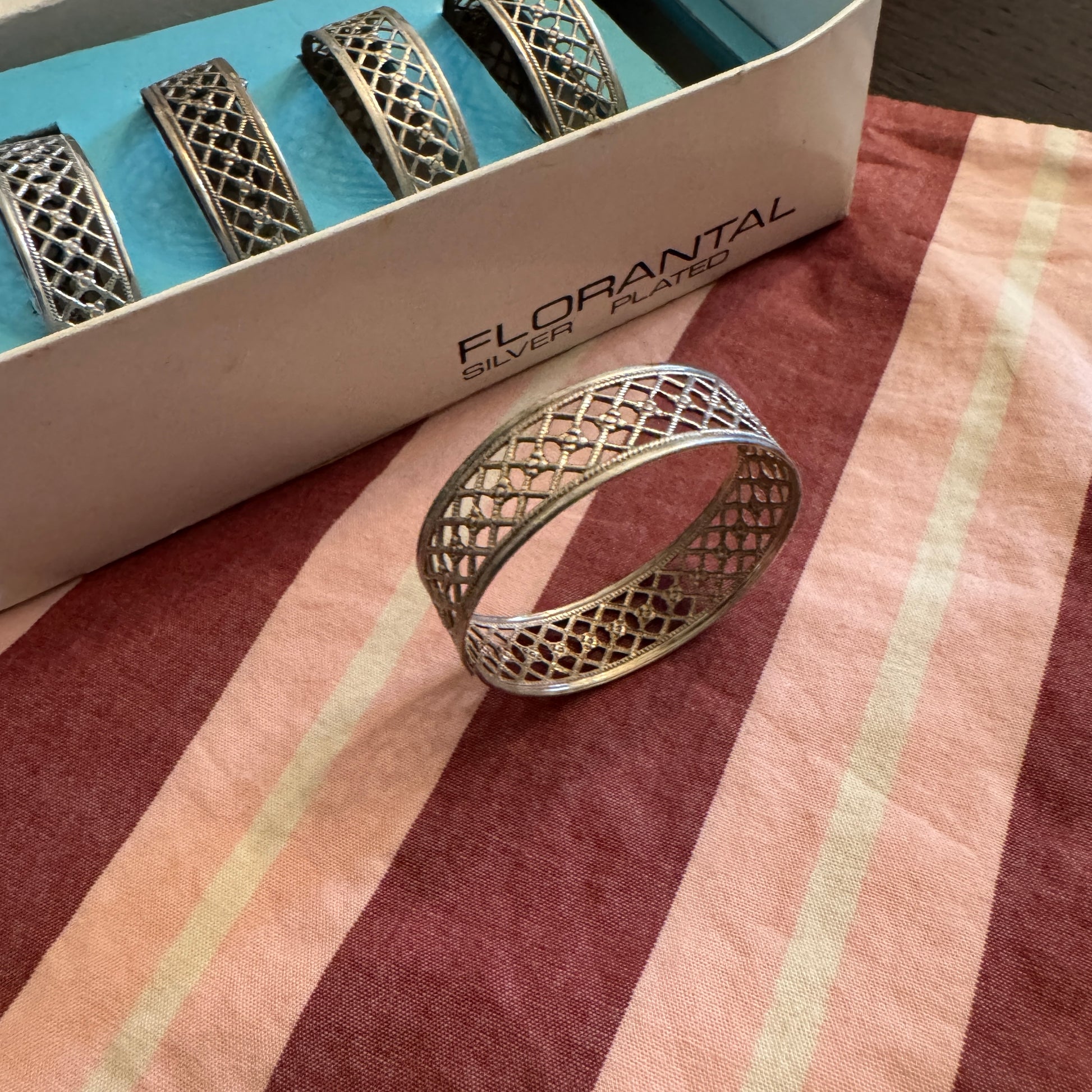 Silver napkin ring with intricate design on a striped fabric background, branded 'Florantal'.