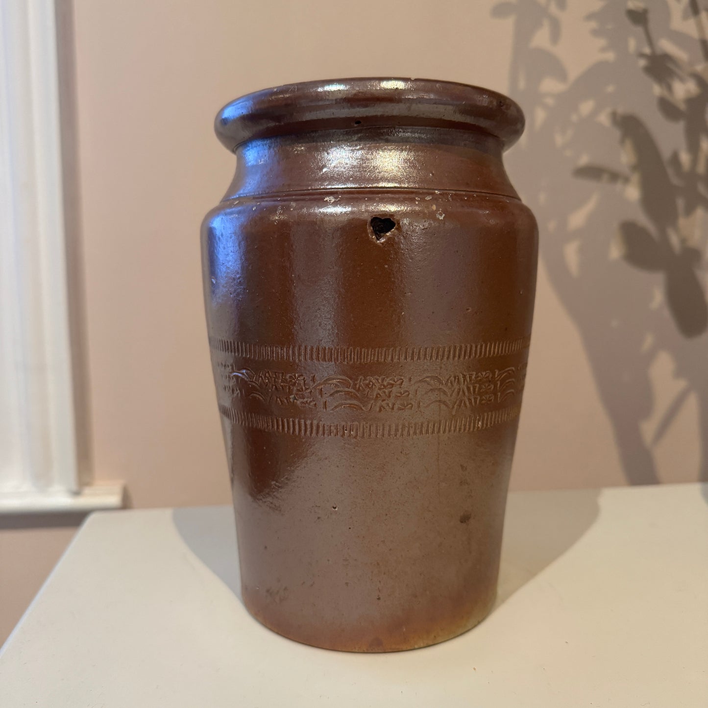 Brown ceramic jar with embossed design on a white surface