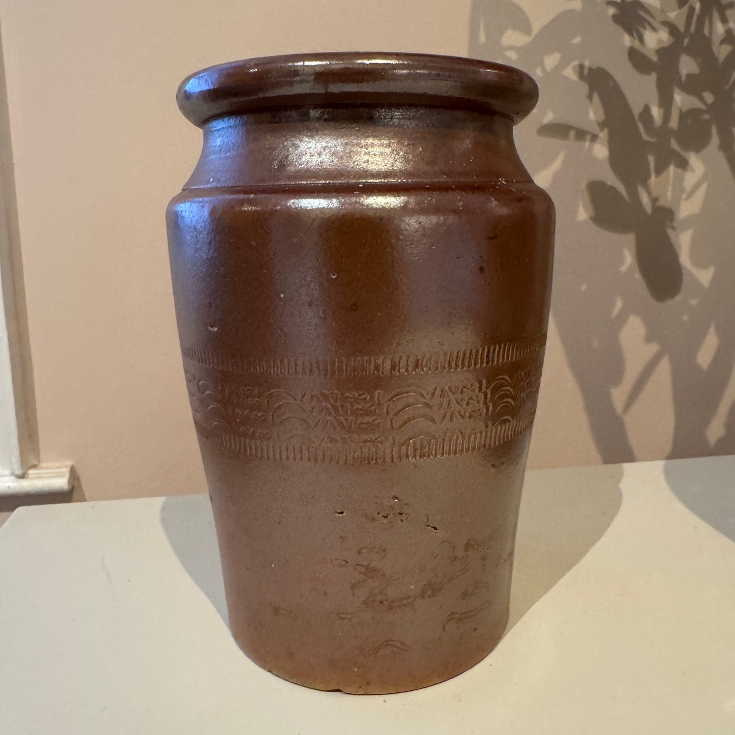 Brown ceramic jar with embossed design on a white surface