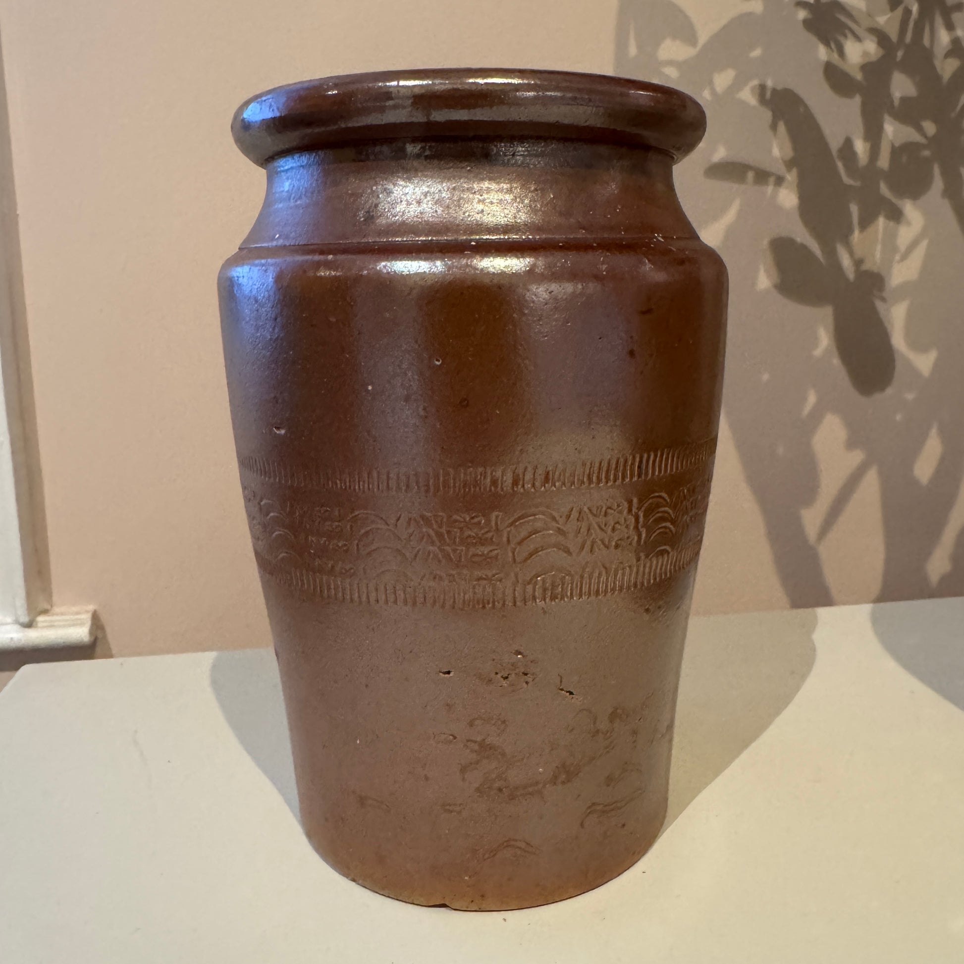 Brown ceramic jar with embossed design on a white surface