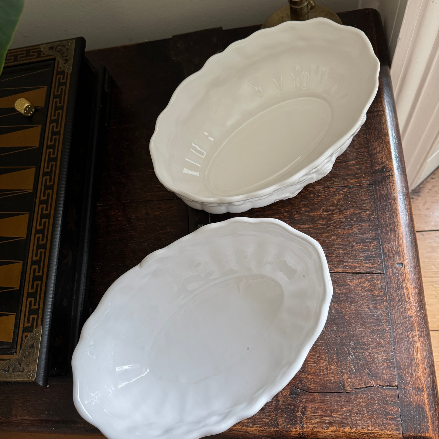 Two white ceramic platters on a wooden surface with a backgammon board in the background.