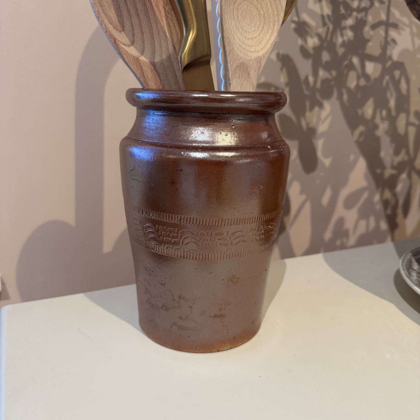 Brown ceramic jar with wooden utensils on a white surface
