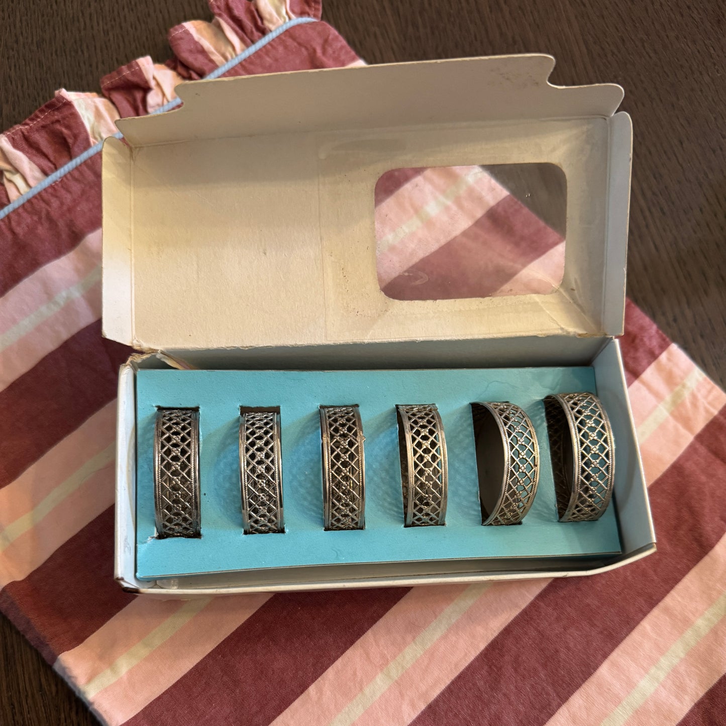 Set of six decorative napkin rings in an open box on a striped fabric background