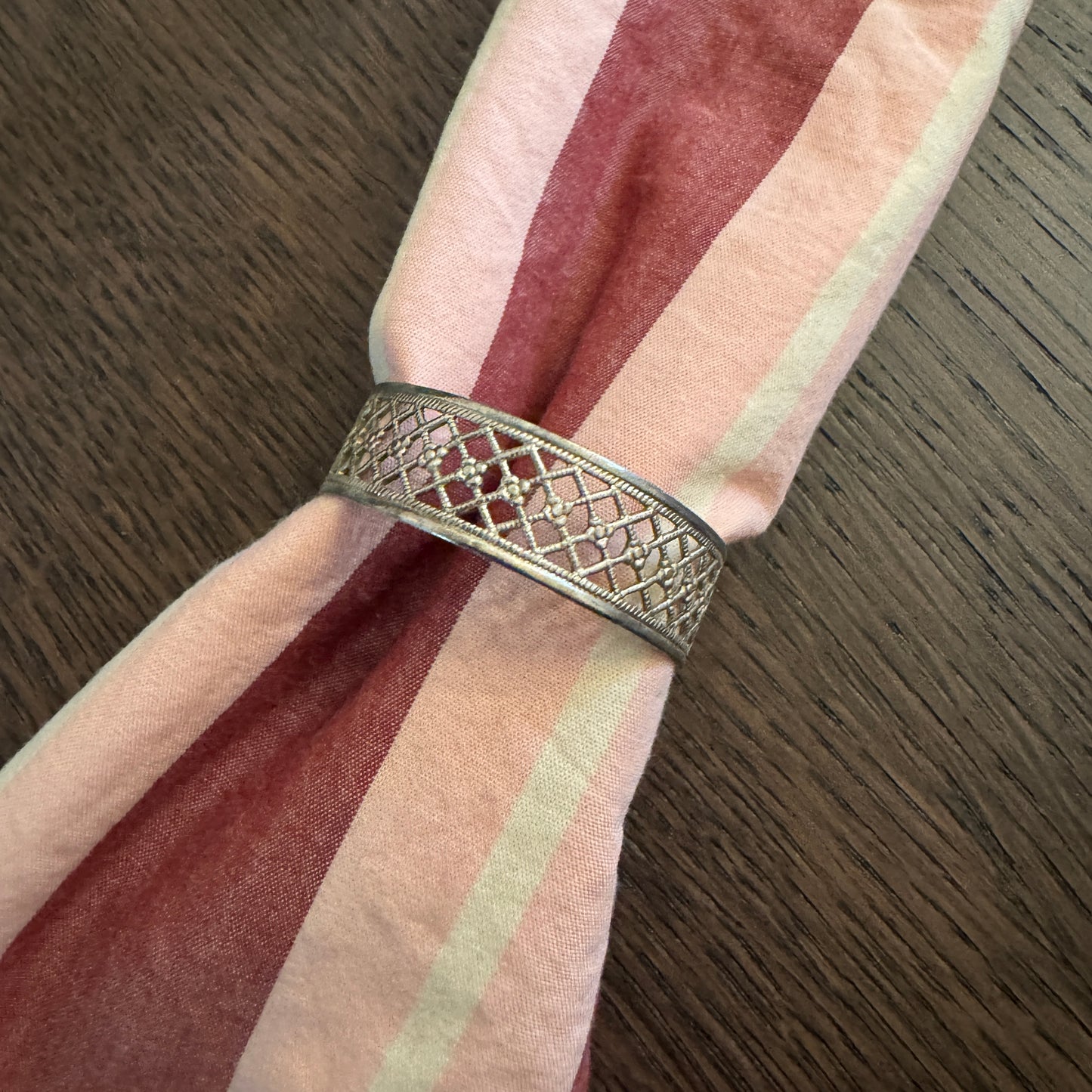 Decorative metal napkin ring on a striped pink and red napkin on a wooden surface