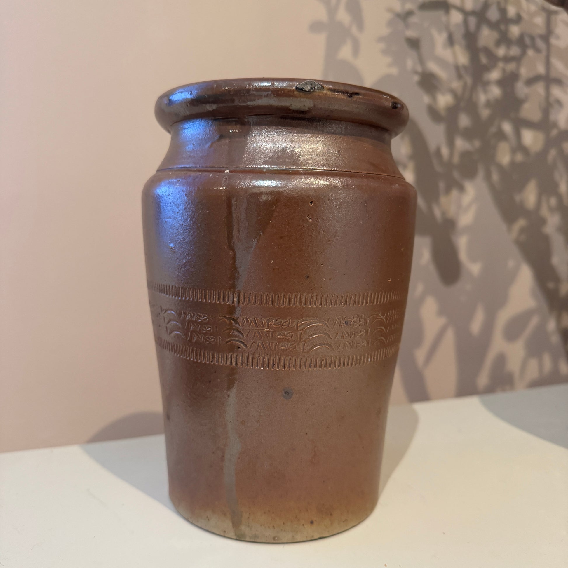 Brown ceramic jar with embossed design on a white surface