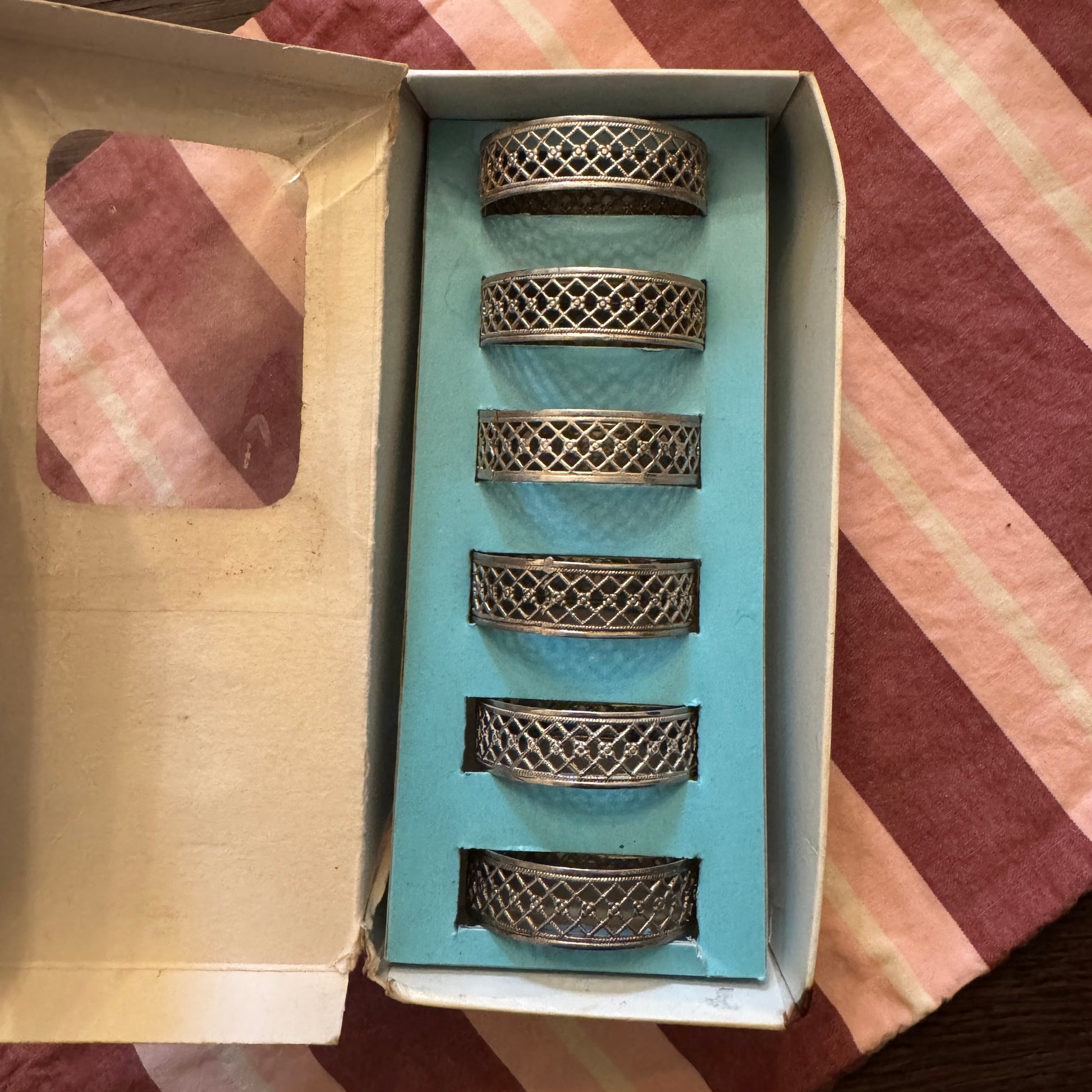 Set of six silver napkin rings in a box on a striped fabric background